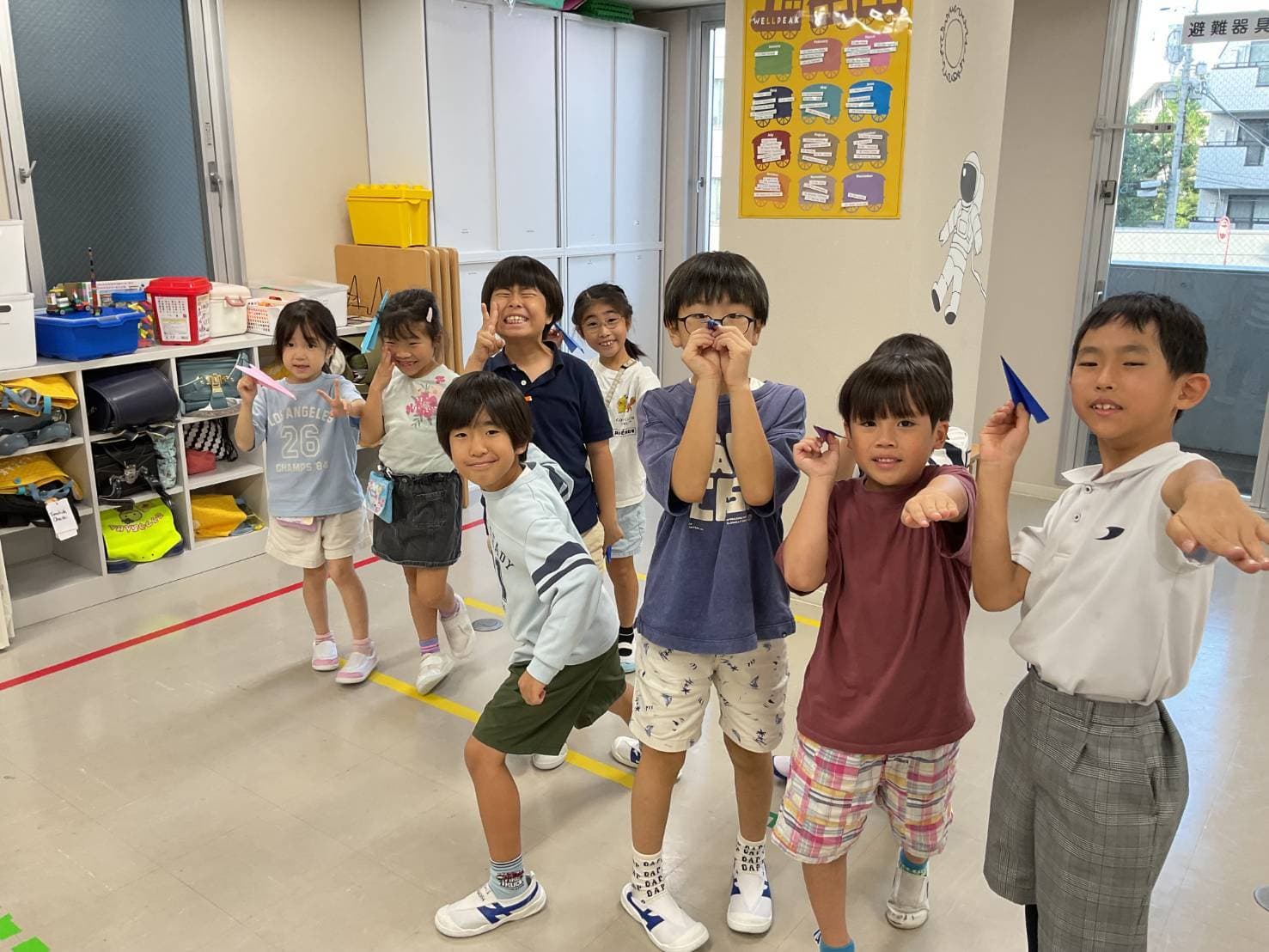 紙飛行機を手にポーズをとる小学生クラスの子どもたち